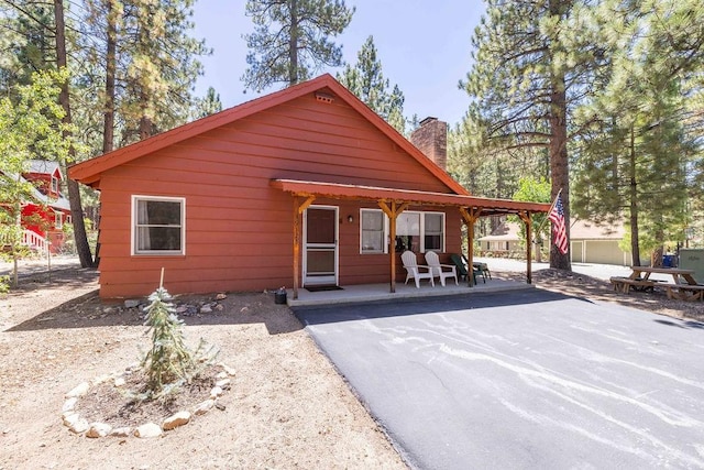 chalet / cabin featuring aphalt driveway, a chimney, and a carport