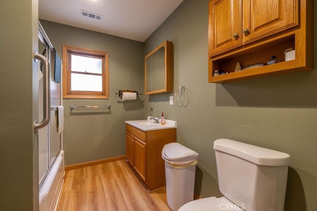 bathroom featuring enclosed tub / shower combo, toilet, wood finished floors, visible vents, and baseboards