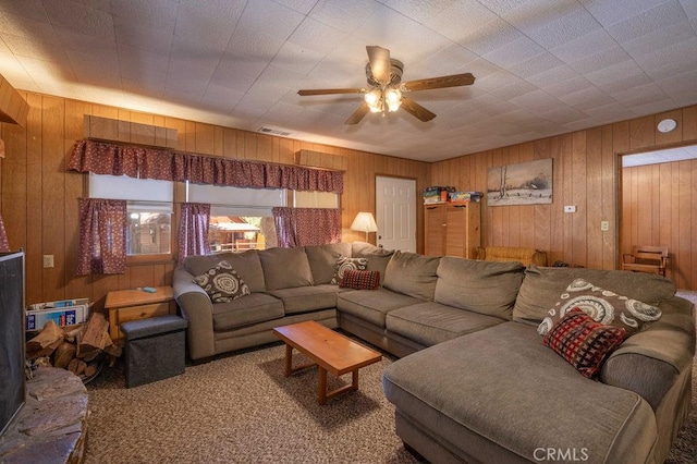 living area with visible vents, a ceiling fan, and wooden walls