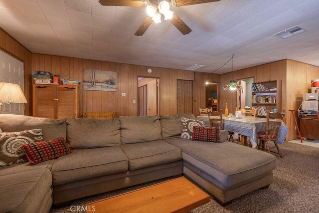 living room with carpet floors, wood walls, visible vents, and a ceiling fan