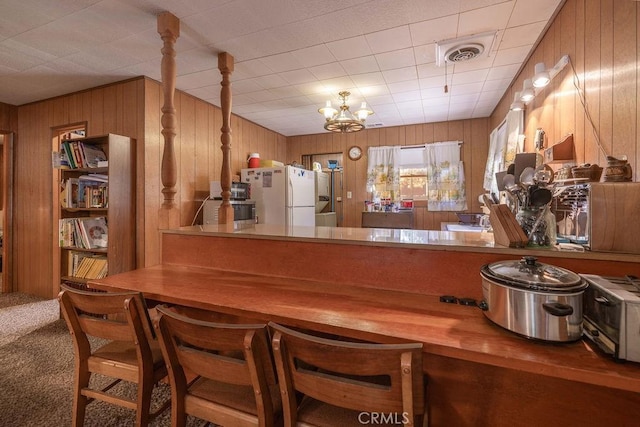 bar with a notable chandelier, wooden walls, carpet flooring, visible vents, and freestanding refrigerator