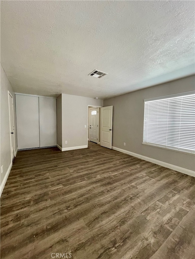 unfurnished bedroom with a closet, a textured ceiling, and dark hardwood / wood-style flooring