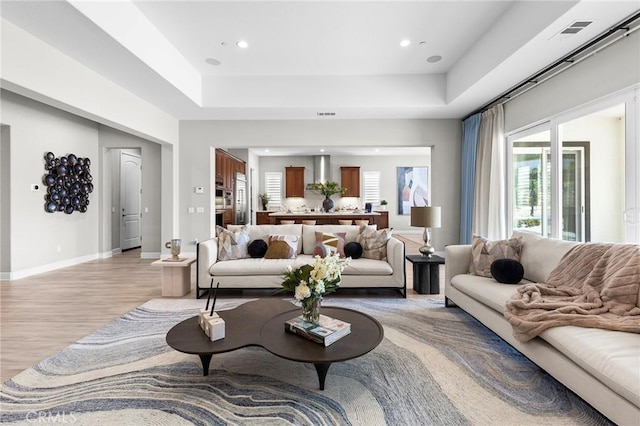 living room with light hardwood / wood-style floors and a raised ceiling