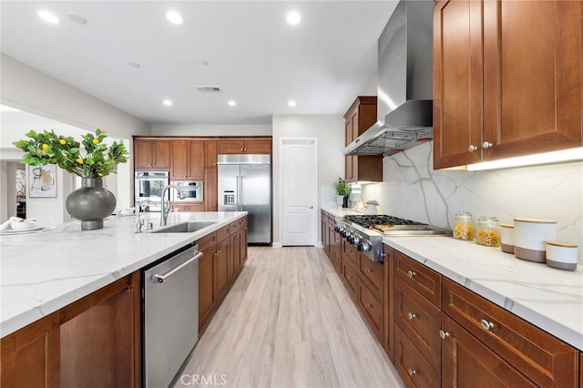 kitchen with sink, stainless steel appliances, light stone counters, and wall chimney range hood