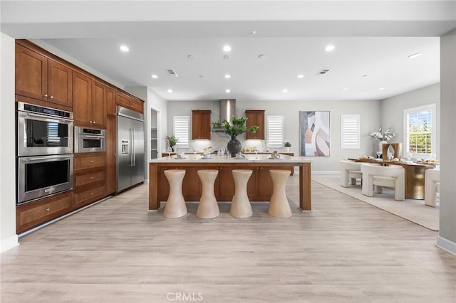 kitchen featuring a breakfast bar area, a kitchen island with sink, stainless steel appliances, and light hardwood / wood-style floors