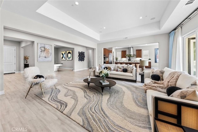 living room featuring light wood-type flooring and a tray ceiling