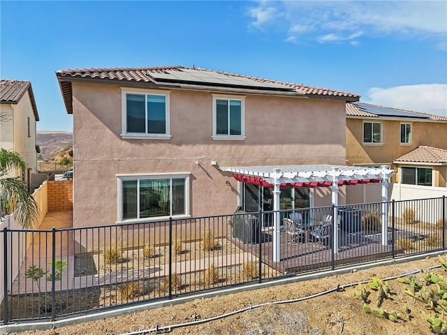 rear view of house featuring a fenced backyard, solar panels, stucco siding, a pergola, and a patio area