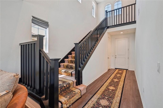 staircase with wood finished floors, a towering ceiling, and baseboards