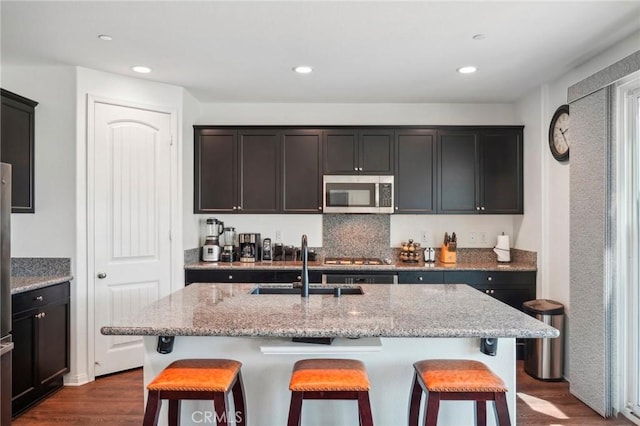 kitchen with stainless steel microwave, a sink, light stone countertops, and a kitchen breakfast bar