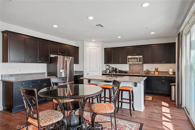 kitchen with light stone counters, dark wood-style flooring, stainless steel appliances, visible vents, and dark brown cabinets