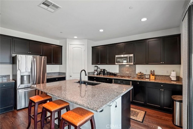 kitchen featuring visible vents, appliances with stainless steel finishes, dark wood-style flooring, light stone countertops, and a sink