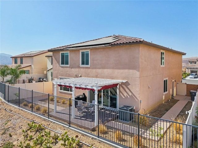 back of house with stucco siding, roof mounted solar panels, a patio area, a pergola, and a fenced backyard