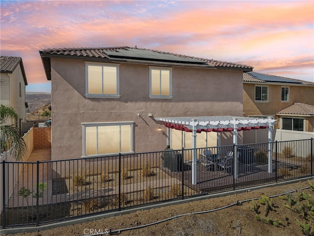 back house at dusk with a pergola and solar panels