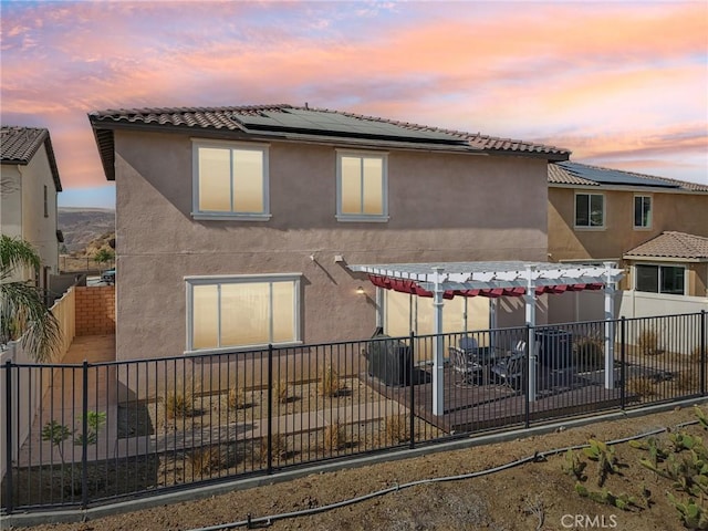 rear view of house featuring a patio, a fenced backyard, solar panels, stucco siding, and a pergola