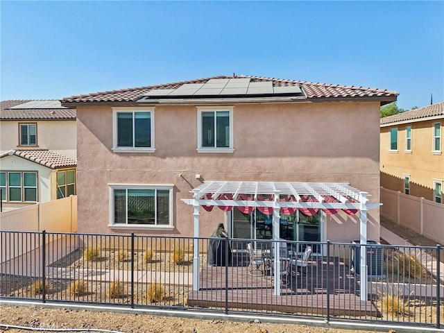 rear view of house with a tiled roof, fence, roof mounted solar panels, and stucco siding