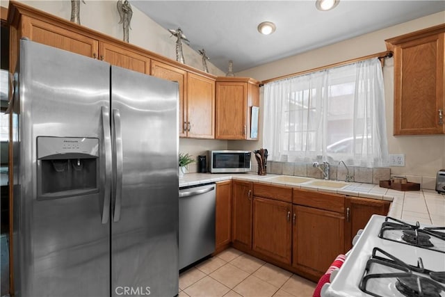 kitchen featuring tile countertops, lofted ceiling, sink, light tile patterned floors, and stainless steel appliances