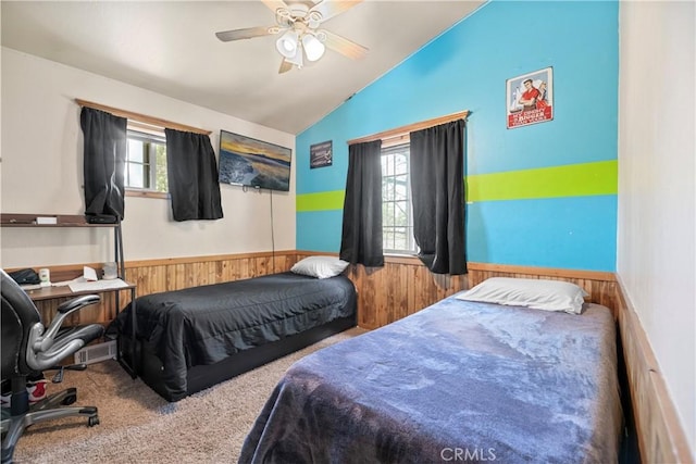 carpeted bedroom with lofted ceiling, ceiling fan, and wood walls