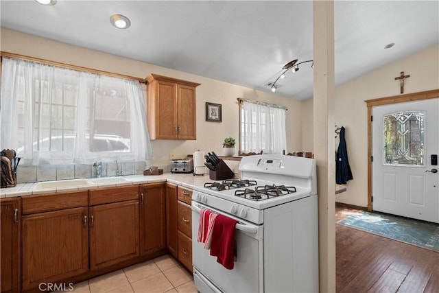 kitchen featuring sink, vaulted ceiling, light wood-type flooring, white gas range, and tile counters