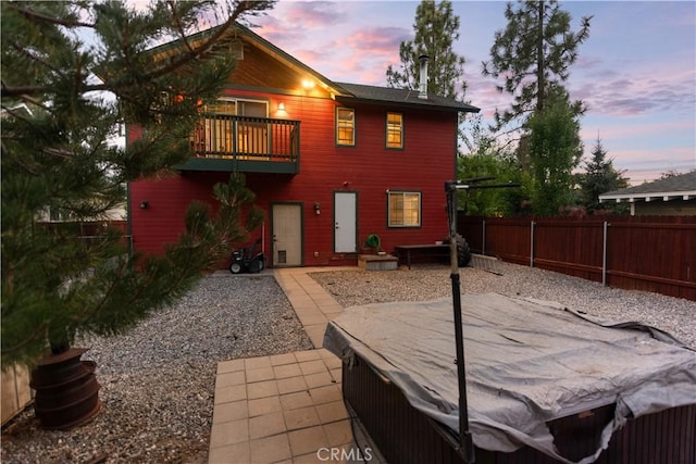 back house at dusk with a balcony and a patio