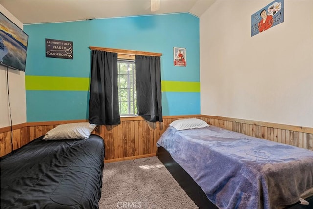 bedroom with lofted ceiling, light colored carpet, and wooden walls