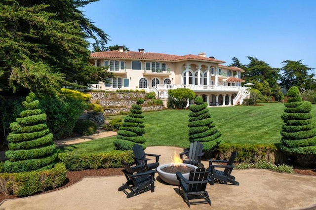 rear view of property with a balcony, a fire pit, a patio area, and a lawn