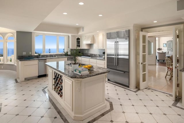 kitchen featuring appliances with stainless steel finishes, custom exhaust hood, a water view, dark stone countertops, and a center island