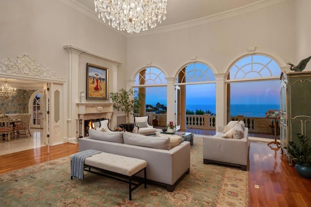 living room featuring ornamental molding, hardwood / wood-style flooring, an inviting chandelier, a water view, and a high ceiling