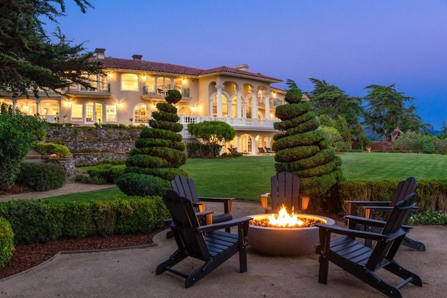 back house at dusk with a yard, a balcony, a patio, and a fire pit