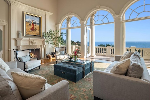 living room featuring a towering ceiling, a premium fireplace, hardwood / wood-style floors, and a water view