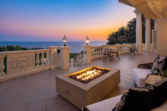 patio terrace at dusk featuring a water view and a fire pit