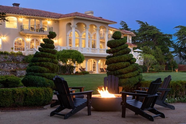 exterior space featuring a lawn, a patio area, a balcony, and an outdoor fire pit