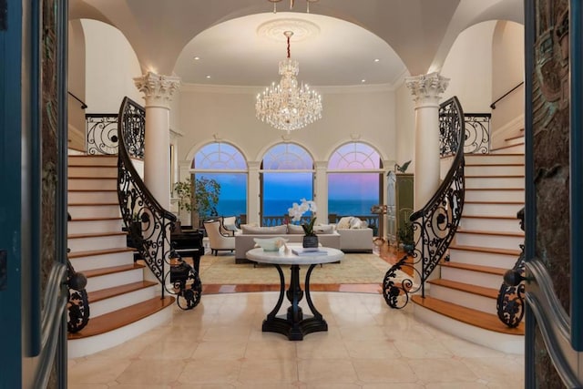 entrance foyer featuring decorative columns, a towering ceiling, a chandelier, and ornamental molding