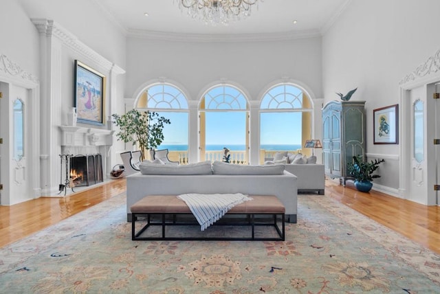 living room featuring a towering ceiling, a water view, light hardwood / wood-style flooring, and ornamental molding