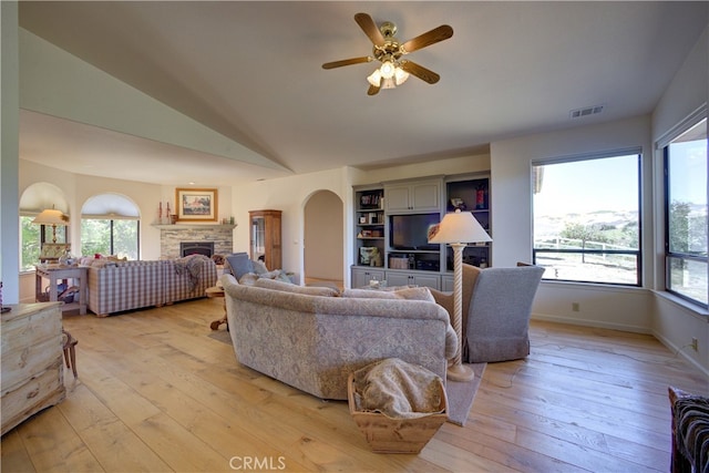 living room with ceiling fan, a stone fireplace, light wood-type flooring, and lofted ceiling