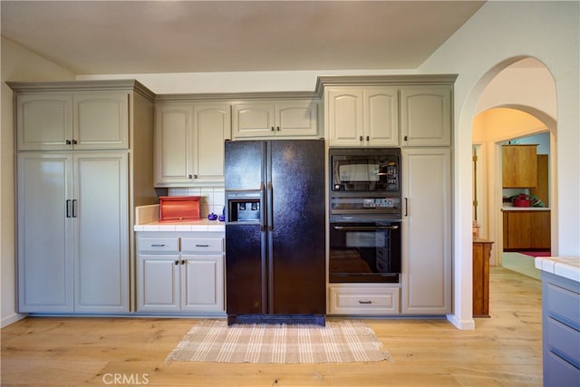 kitchen featuring decorative backsplash, light wood-type flooring, black appliances, and tile countertops