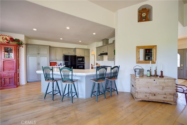 kitchen with kitchen peninsula, black appliances, light hardwood / wood-style floors, and a breakfast bar area