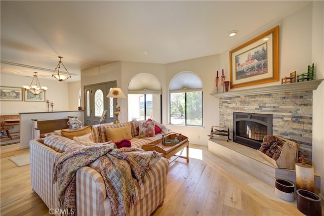 living room featuring an inviting chandelier, light hardwood / wood-style floors, and a stone fireplace