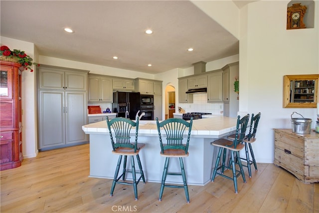 kitchen featuring light wood-type flooring, tasteful backsplash, kitchen peninsula, a kitchen breakfast bar, and black appliances