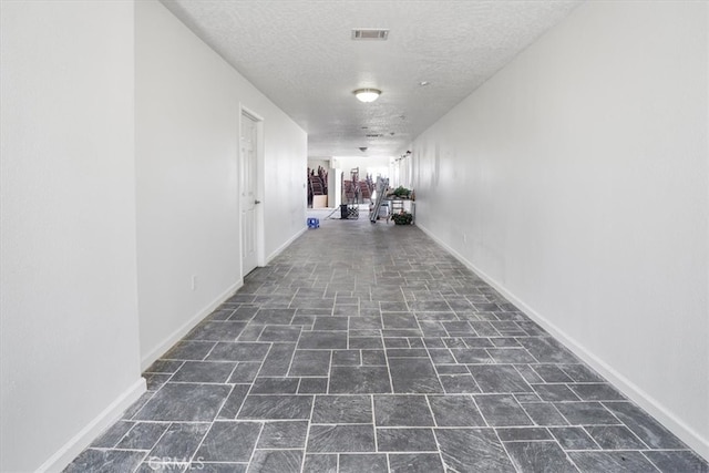 hall with dark tile patterned flooring and a textured ceiling