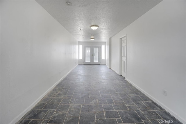 corridor featuring french doors, a textured ceiling, and dark tile patterned floors