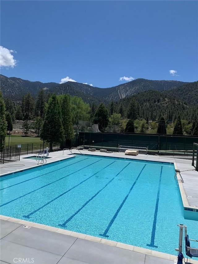 community pool with fence, a wooded view, and a mountain view