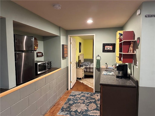 kitchen with dark countertops, wood finished floors, a sink, stainless steel microwave, and freestanding refrigerator