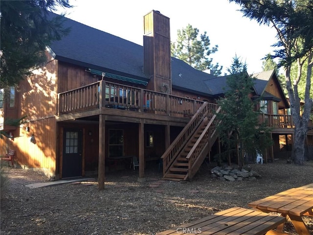 rear view of house with a wooden deck, a shingled roof, and a chimney