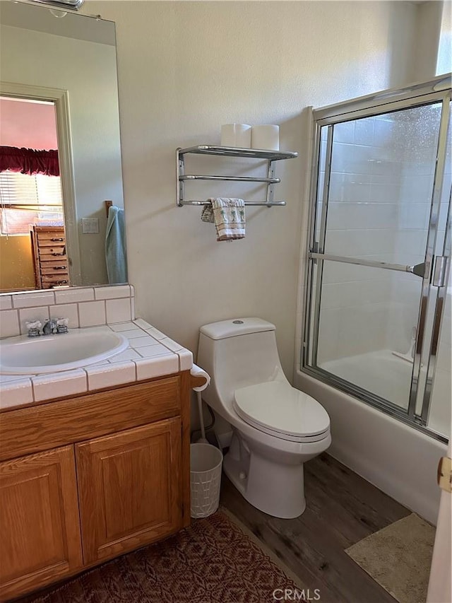 full bathroom with hardwood / wood-style flooring, vanity, toilet, and bath / shower combo with glass door