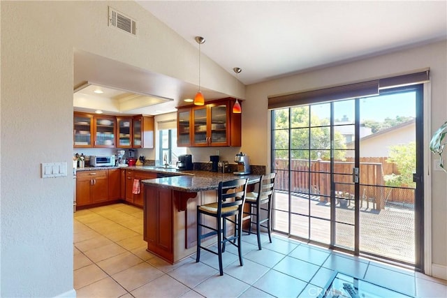 kitchen with dark stone countertops, hanging light fixtures, kitchen peninsula, light tile patterned floors, and a breakfast bar area