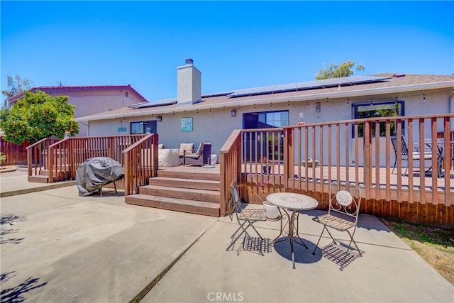 rear view of property featuring a wooden deck, a patio area, and solar panels