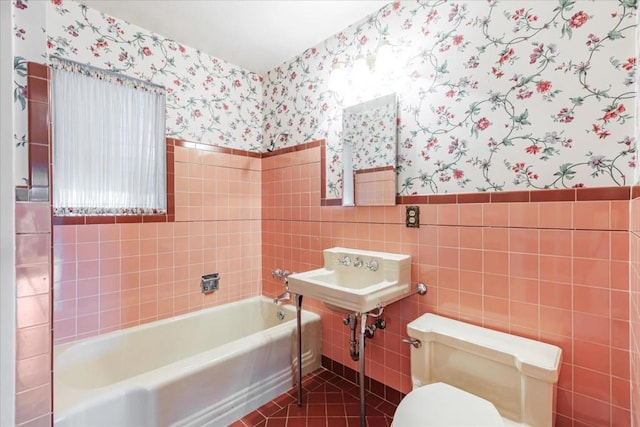 bathroom with toilet, tile patterned flooring, tile walls, and a washtub