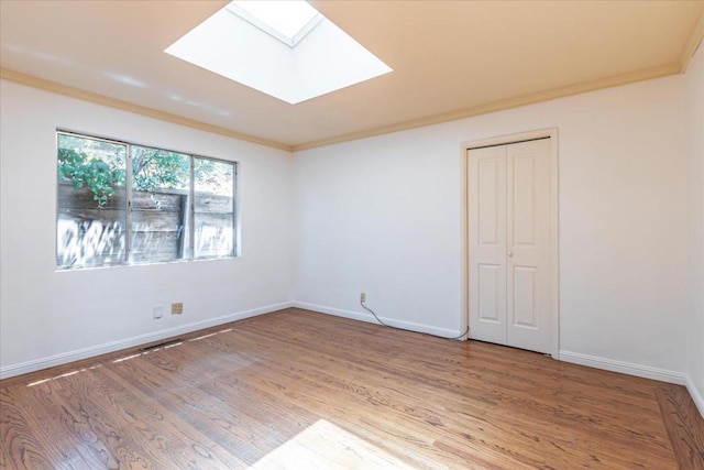 empty room with ornamental molding, a skylight, and hardwood / wood-style floors