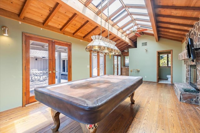 rec room with french doors, a stone fireplace, pool table, vaulted ceiling with skylight, and light hardwood / wood-style floors