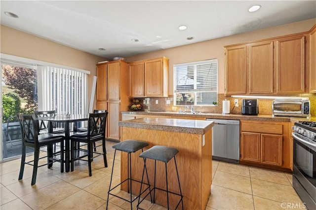 kitchen featuring backsplash, a center island, light tile patterned floors, appliances with stainless steel finishes, and a kitchen breakfast bar